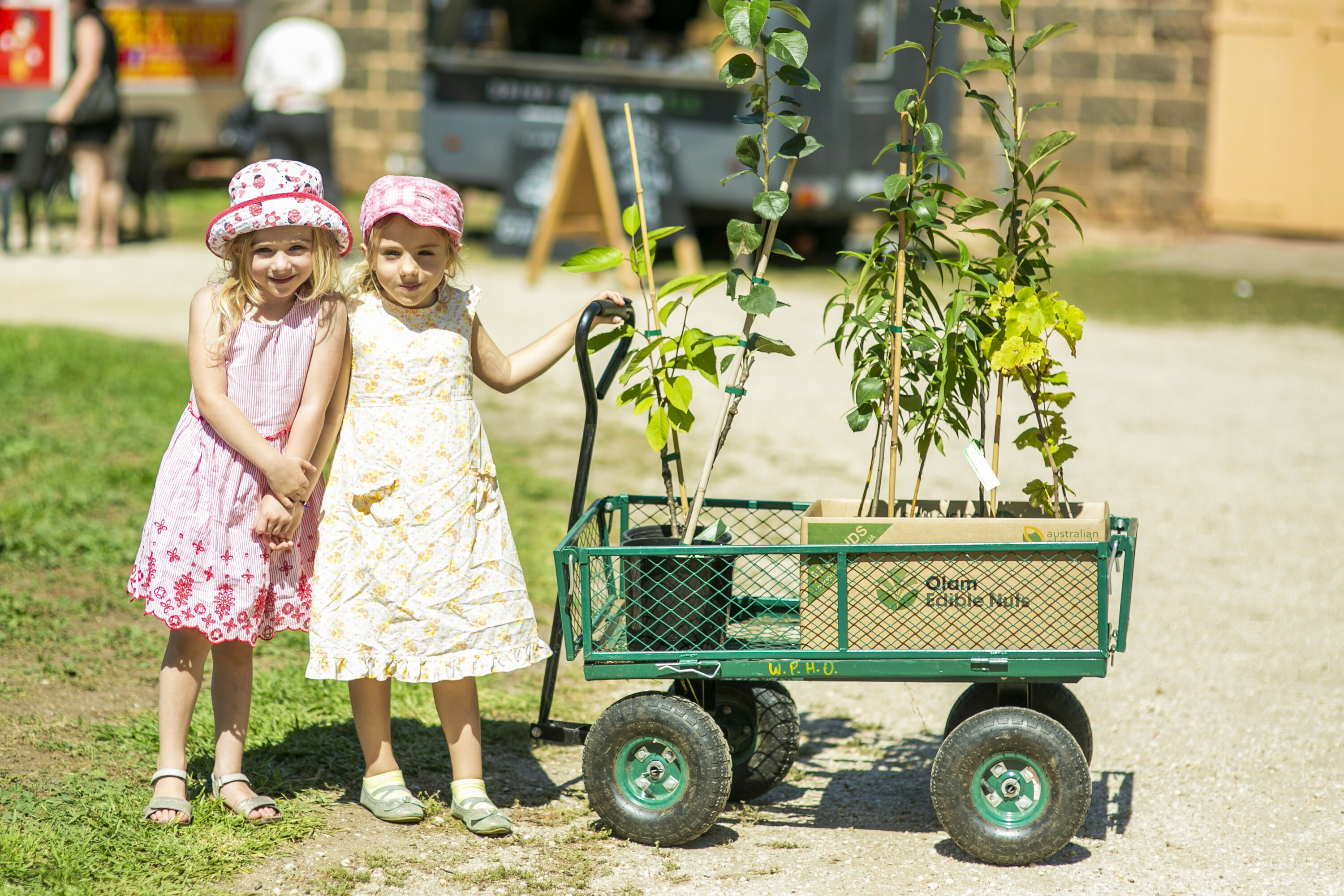 two children smiling and holding a buggy with fruit trees inside