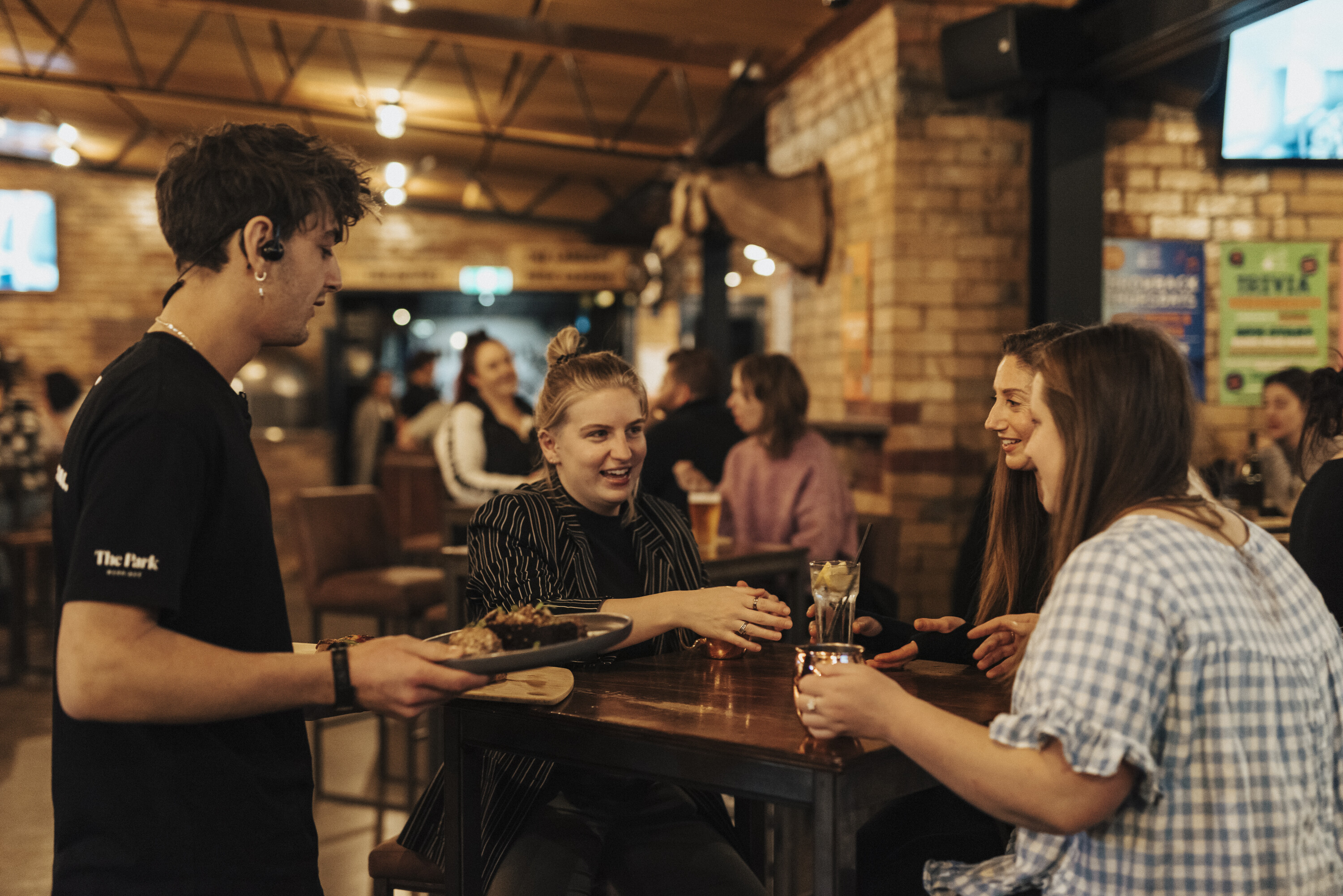 waiter handing plate of food to women seated at a table in bar