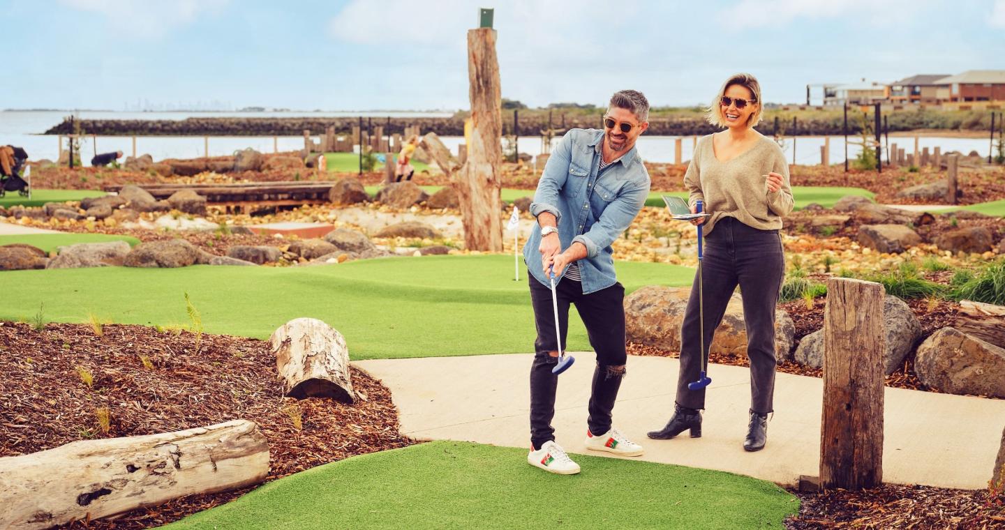 two adults playing mini golf with the ocean in the background