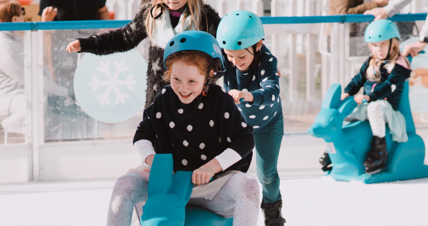 children wearing ice skates using kangaroo skating aid