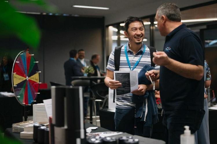 two adults one with a lanyard talking in a corporate setting