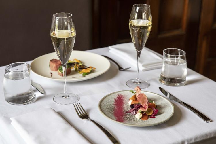 a close up of entrees and two glasses of sparkling wine on a white table cloth