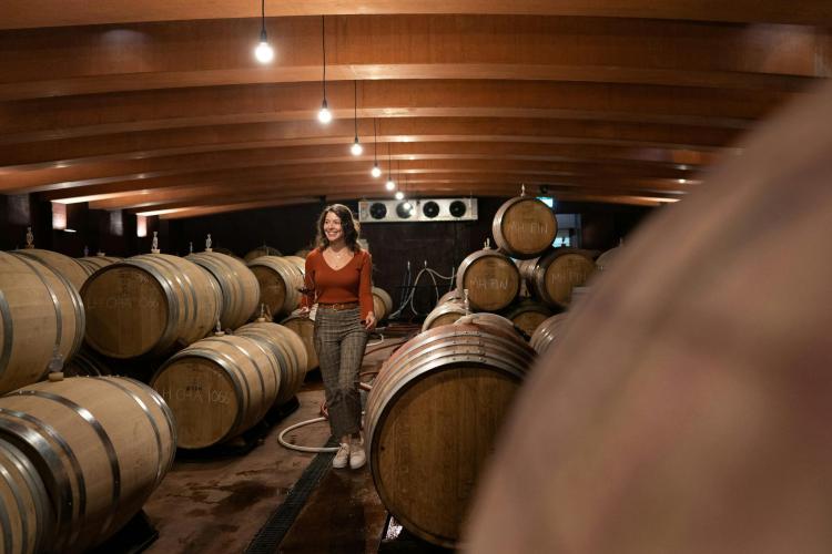 Adult walking through underground barrel room with glass of wine