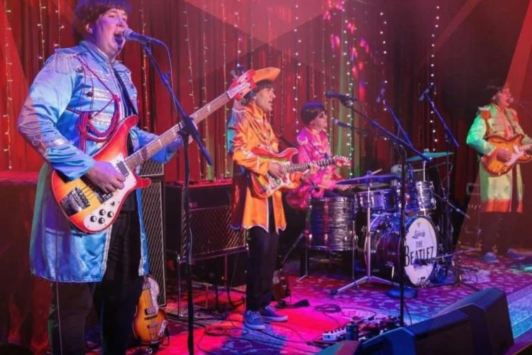 4 band members playing musical  instruments and singing on stage