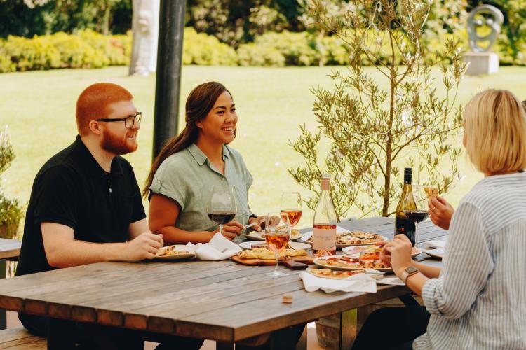 adults seated outdoors with wine and pizza