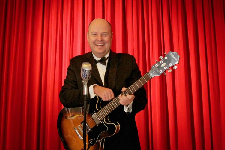 Smiling man holding a guitar - red curtains in background
