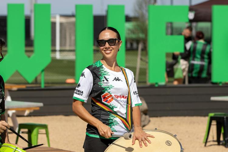 a woman drumming and smiling to camera with a Western United FC jersey on