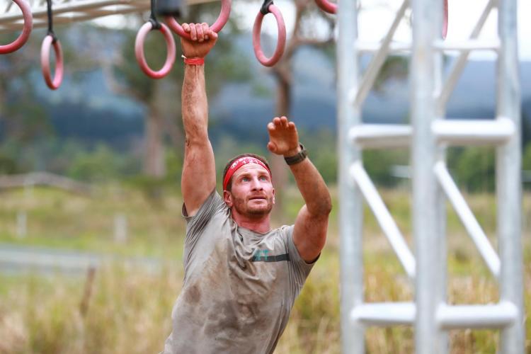 Male spartan participant swinging on an obstacle