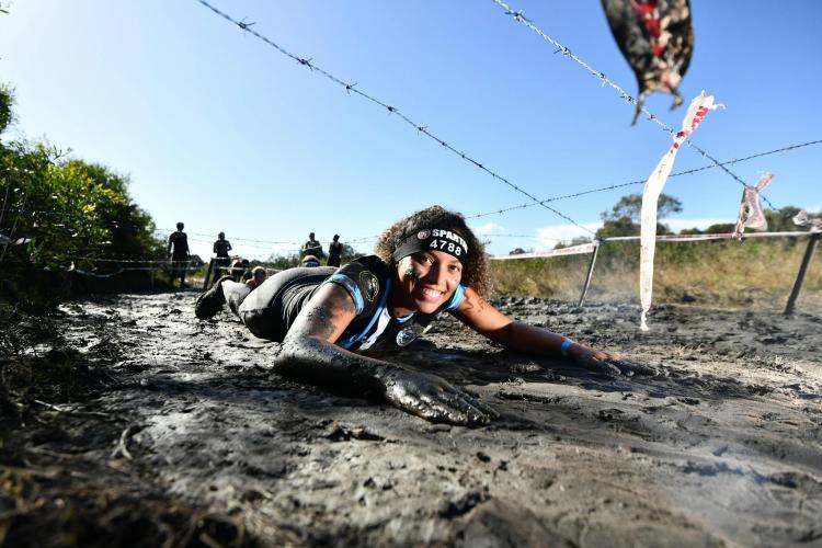 Female Spartan participant crawls through mud