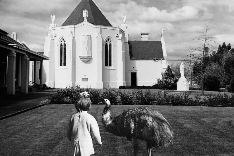 A black and white photo of a child and an emu standing before an old church building.