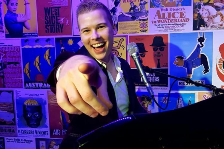 Smiling man sitting at a piano and pointing a finger