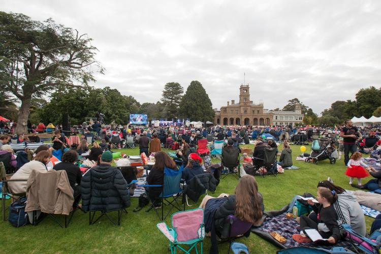 crowd seated on lawn in front of Werribee Park Mansion watching performance