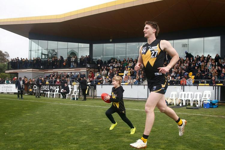 Player in Werribee Football Club jersey running out onto ground with child