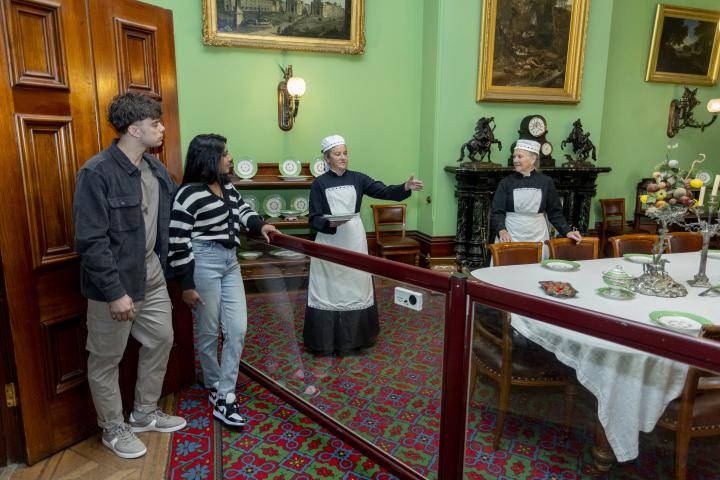 two adults chatting to volunteers dressed up in historical costume inside Werribee Park Mansion